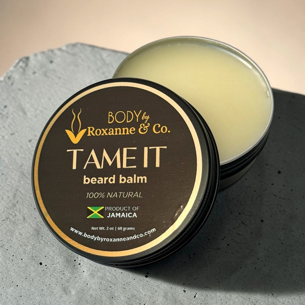 Beard balm container labeled 'Tame It' by Roxanne & Co. on a textured surface.