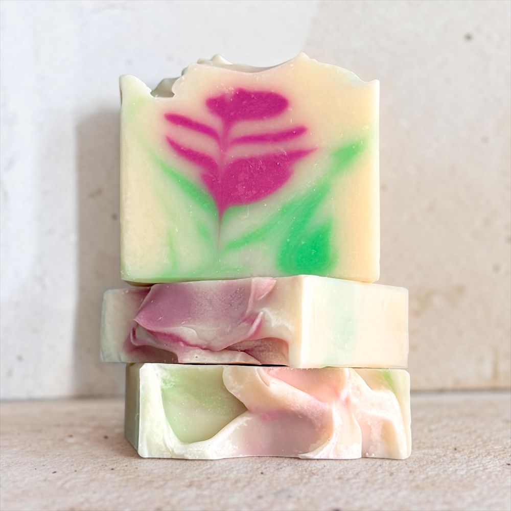 Three stacked handmade soap bars with a marbled cream base, green and pink swirls, and a pink floral design on the top bar, set against a neutral light beige background.