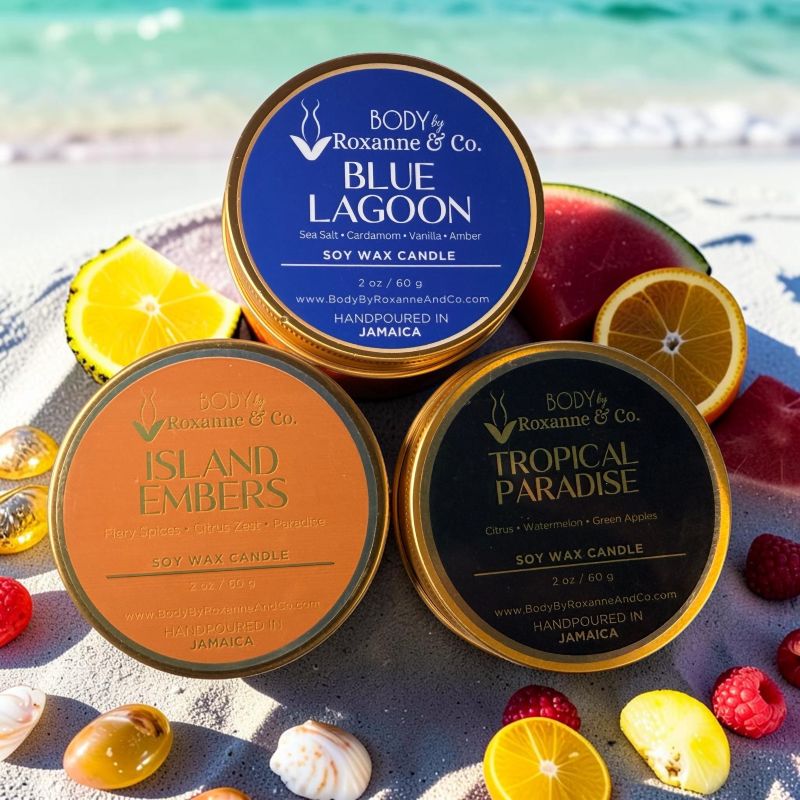 BODY By Roxanne & Co. Tropical Trio soy candle set in gold tins, featuring Blue Lagoon, Island Embers, and Tropical Paradise scents on a sandy beach.
