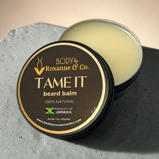 Beard balm container labeled 'Tame It' by Roxanne & Co. on a textured surface.