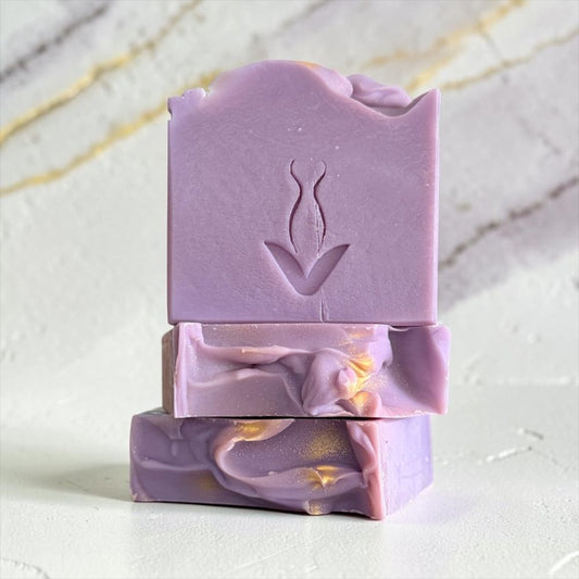 Three stacked lavender soap bars with a botanical leaf design embossed on the top bar, set against a light marble background.