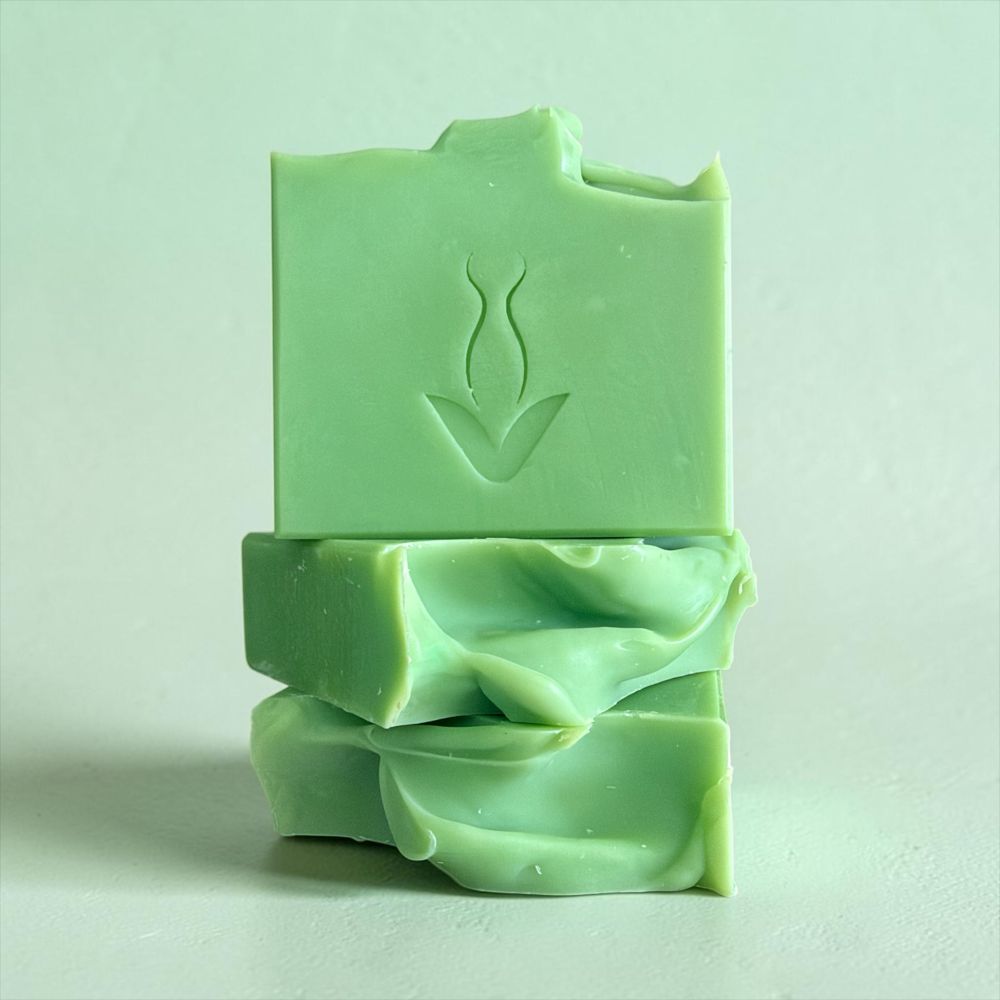 Three stacked bars of light green handmade soap on a light green background, with the top bar embossed with a simple botanical leaf design.