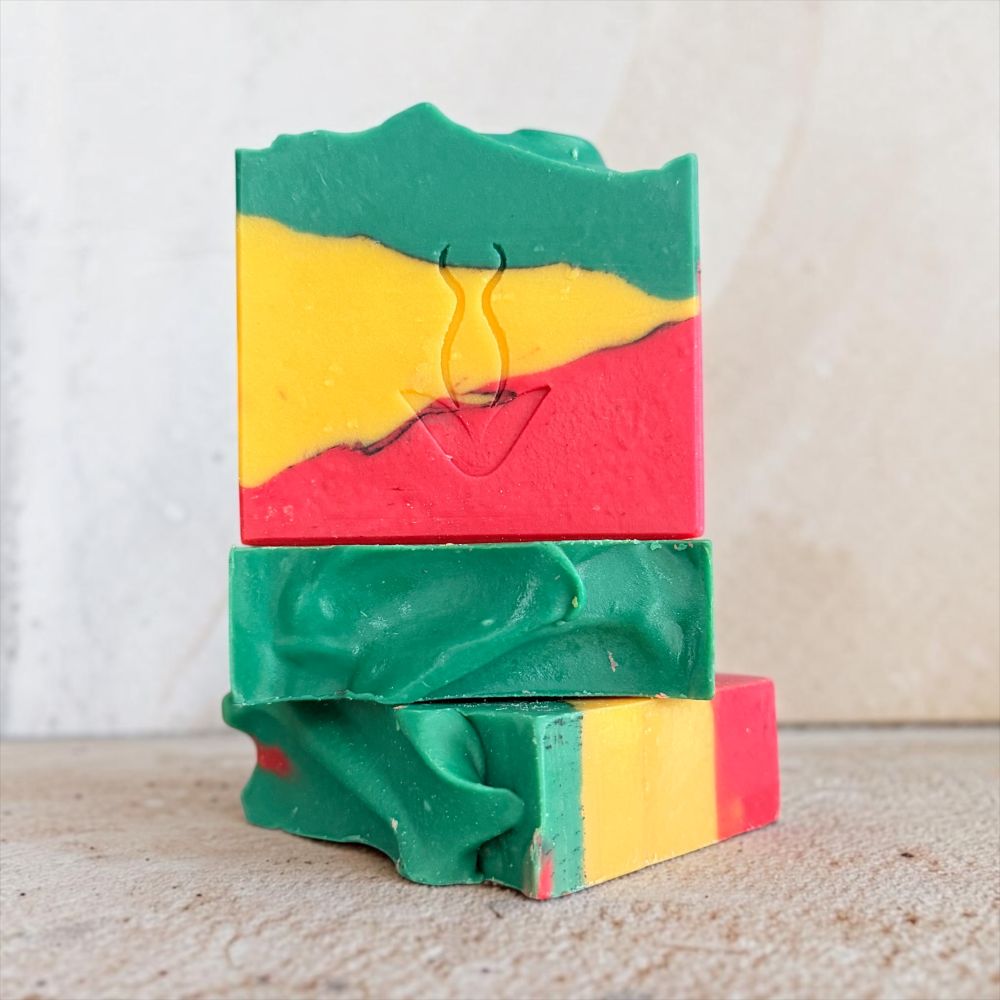 Three stacked rectangular bars of handmade soap with a swirled pattern of green, yellow, and red, featuring a small embossed heart design on the top bar.