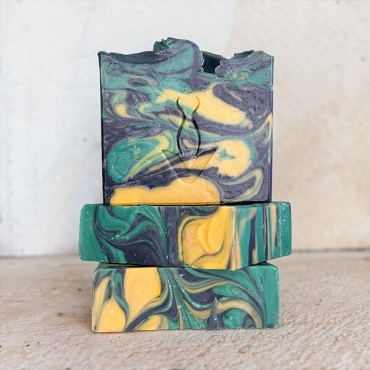Three stacked handmade soap bars with a marbled swirl pattern of green, yellow, and dark gray, photographed against a neutral light beige background.