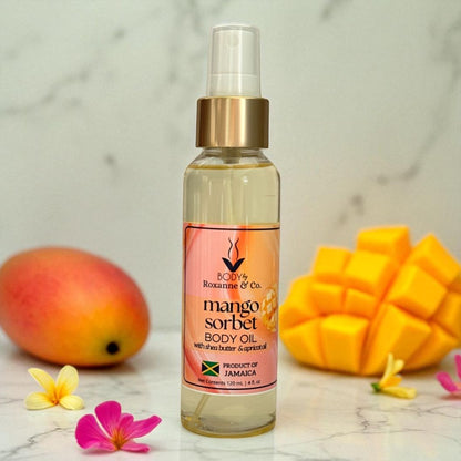 Bottle of mango sorbet body oil with mangoes and flowers on a marble surface