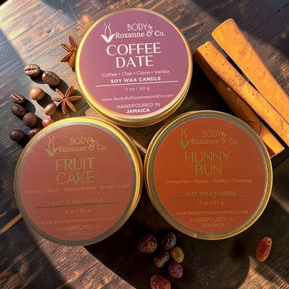 Three scented candles from Body by Roxanne & Co. on a wooden surface with spices and fruits.