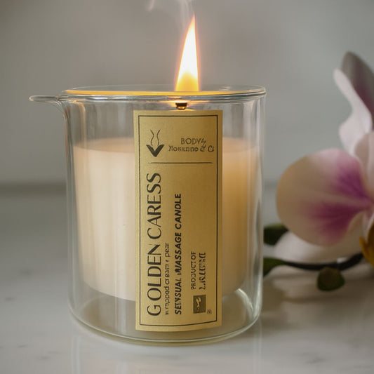 MassageCandleGoldenCaress in a glass jar with a label, next to an orchid flower on a neutral background