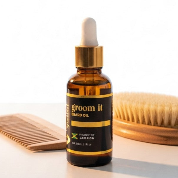 A 30 ml amber glass dropper bottle of groom it Beard Oil, styled on a white surface with a wooden comb on the left and a wooden brush on the right.